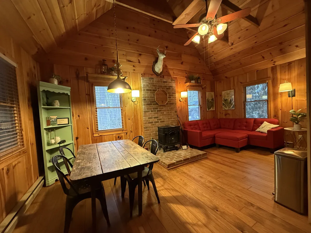 Inside, the red sectional couch, rustic dining table, and brick fireplace create a warm setting. The wood accents and inviting furnishings evoke feelings of comfort and connection, ideal for relaxing evenings after a day of exploring.