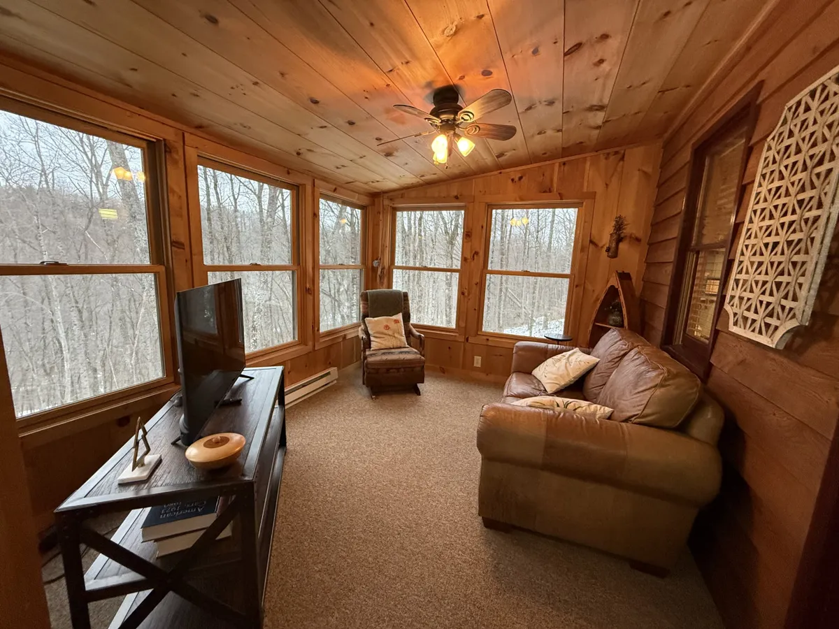 This image captures a sunlit living space with large windows, comfortable seating, and wood paneling, offering a view of the outdoors. The space is bathed in natural light, suggesting a serene place to relax and take in the beauty of the mountains.